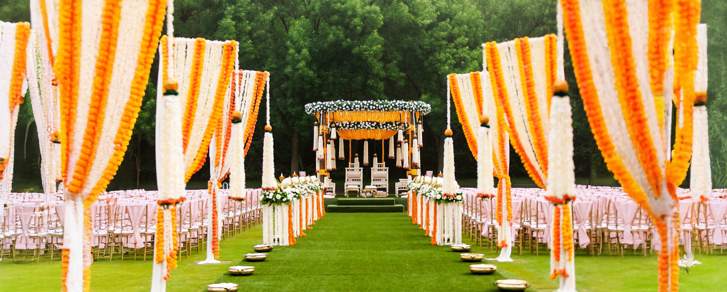 Outdoor wedding mandap decorated with marigold and jasmine garlands on a lush green lawn for a destination wedding.