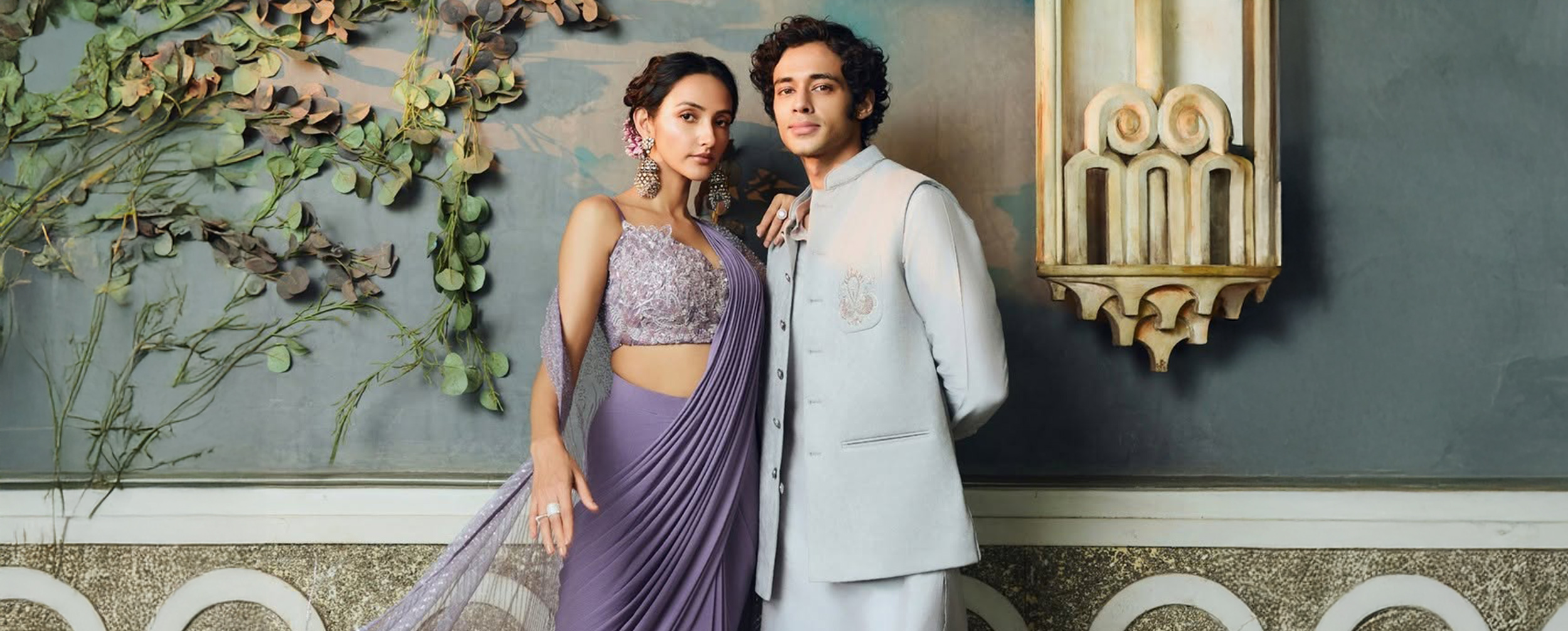 Couple in stylish festive outfits &ndash; woman in a lavender designer saree and man in pastel ethnic wear &ndash; perfect Ganesh Chaturthi 2025 celebration look.