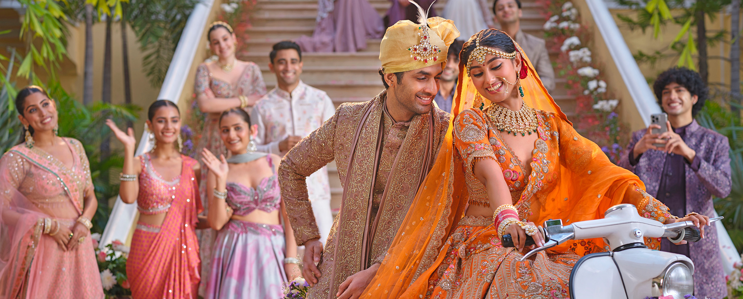Bride wearing elegant orange lehenga, riding scooter with groom behind her 