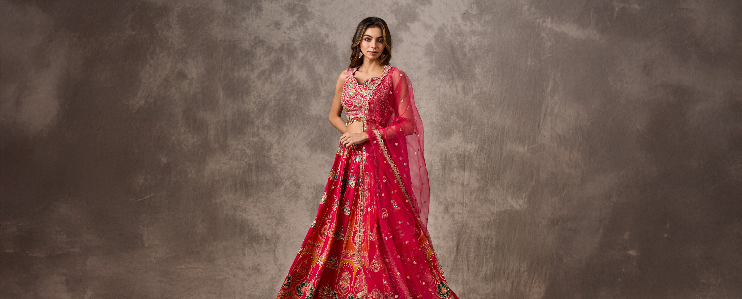 Woman posing in a bright pink and orange patterned lehenga skirt with a matching embroidered blouse.