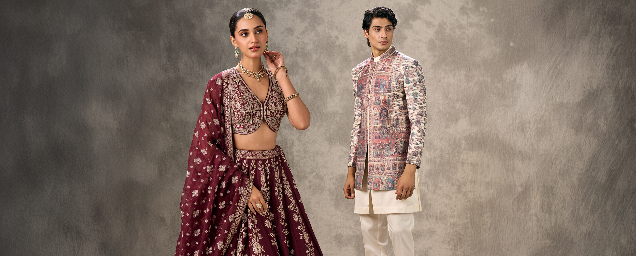 Stylish couple in traditional Navratri outfits &mdash; woman in a maroon embroidered lehenga choli with dupatta, and man in a cream churidar with a printed sherwani jacket &mdash; perfect for Garba and Dandiya celebrations.